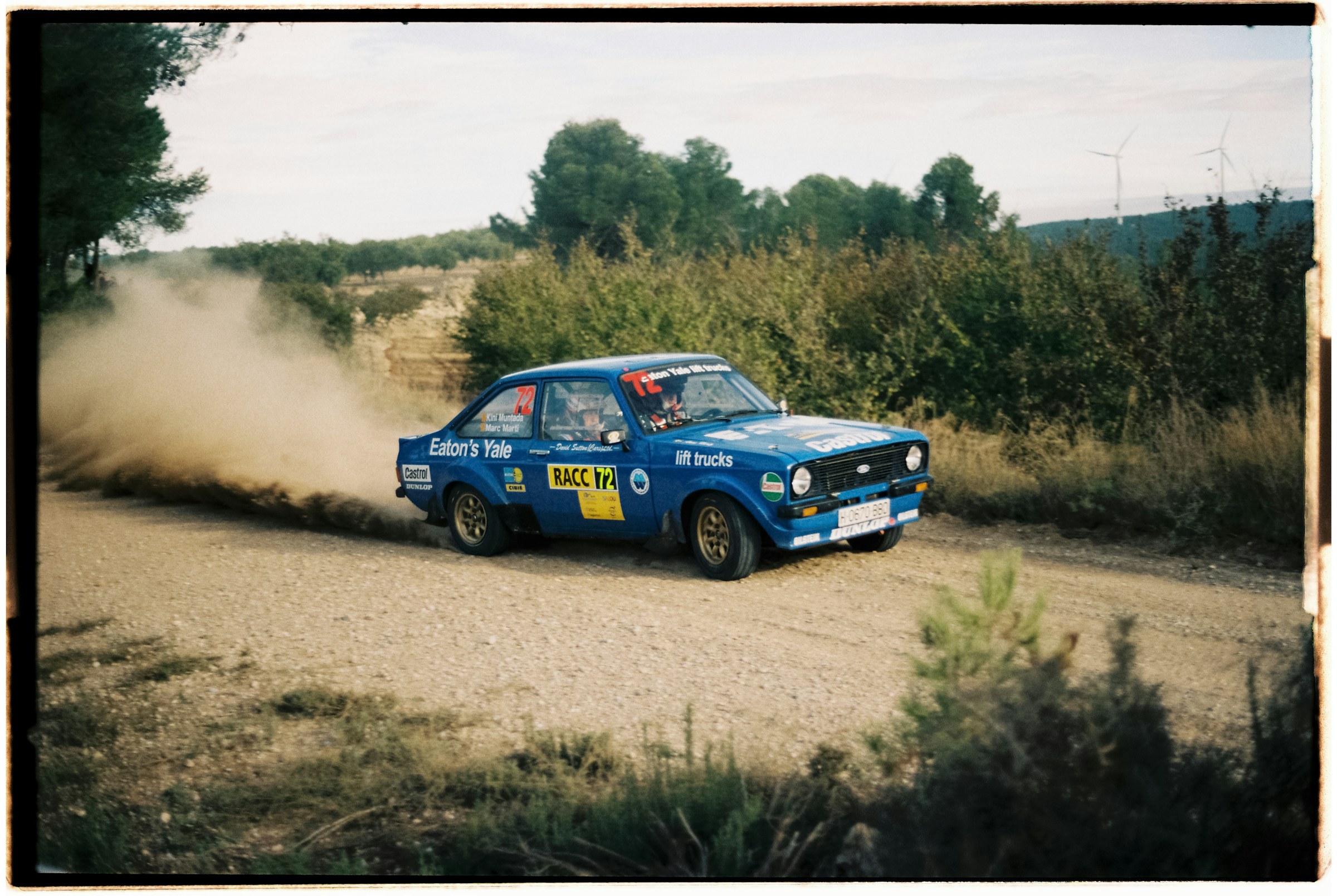 A classic rally car drifting through a cloud of dust