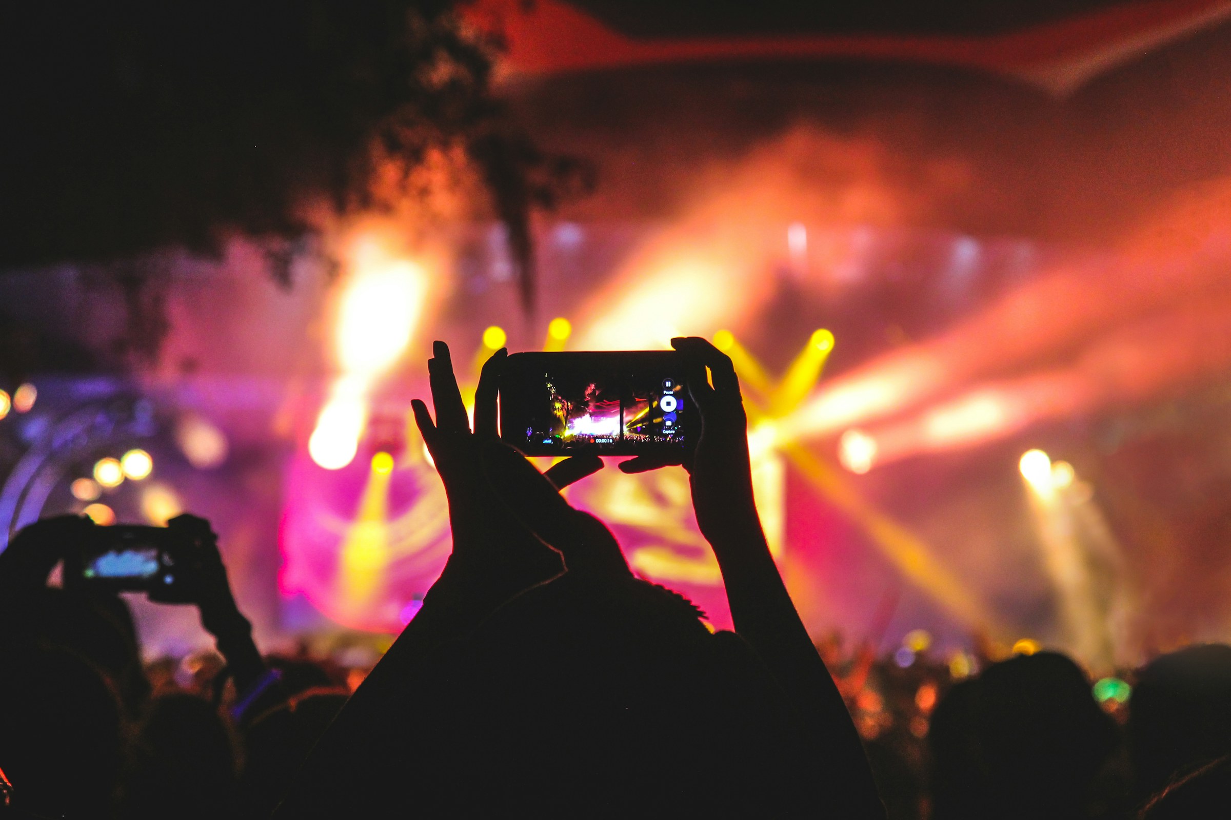 A fan filming a concert on a phone amid stage lights